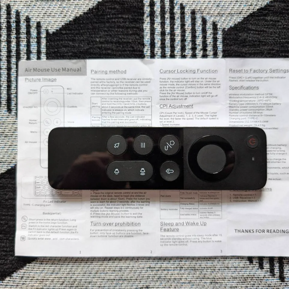 A glossy black Air Mouse remote lying on its printed manual on a black and white patterned rug.