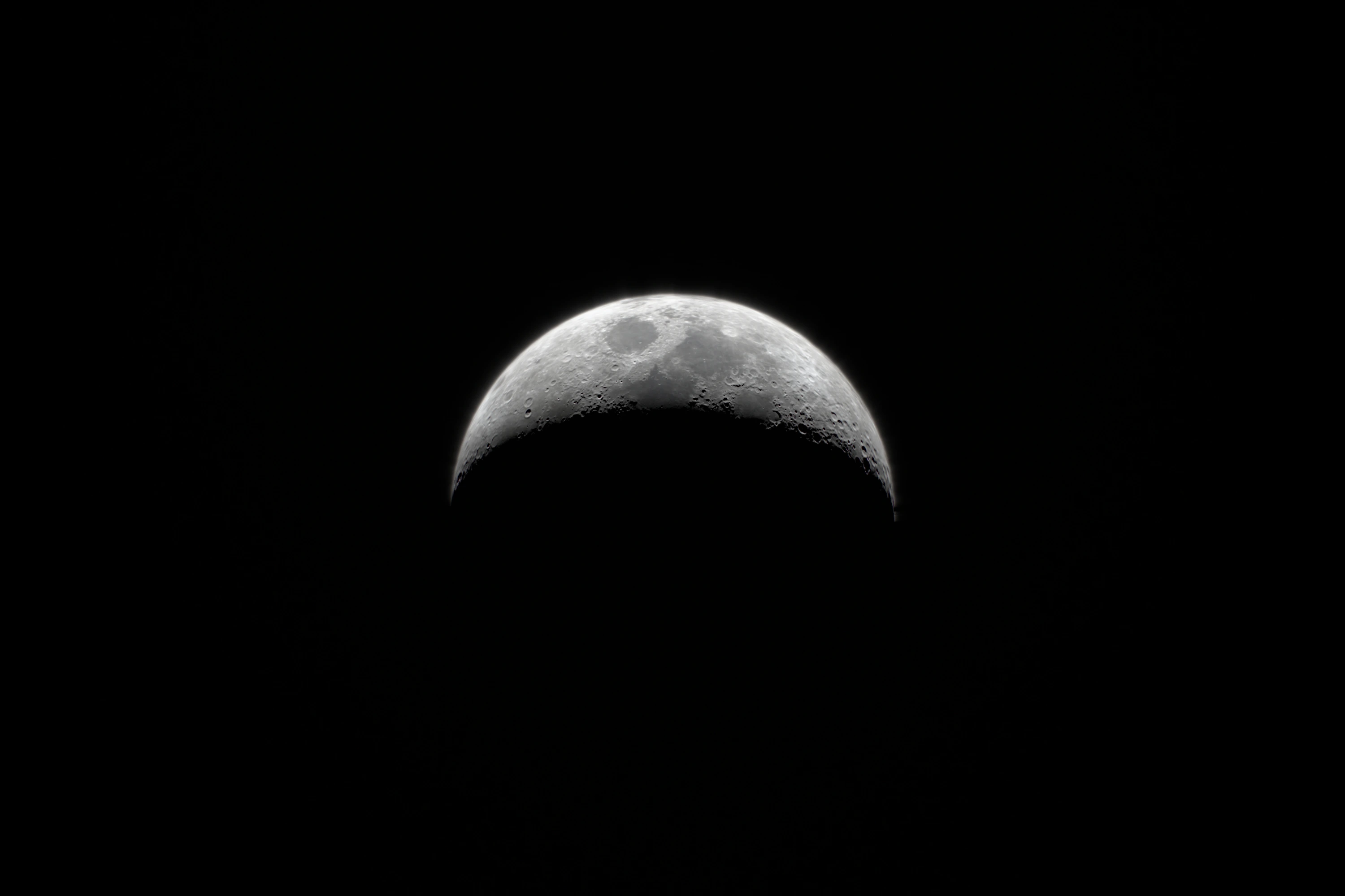 A thin crescent Moon at 50× on black, with maria, craters and rough relief along the terminator.