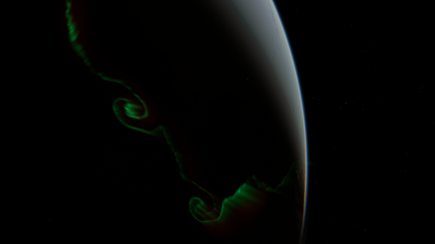 A view from above: only thin green outlines curl over the dark Earth.